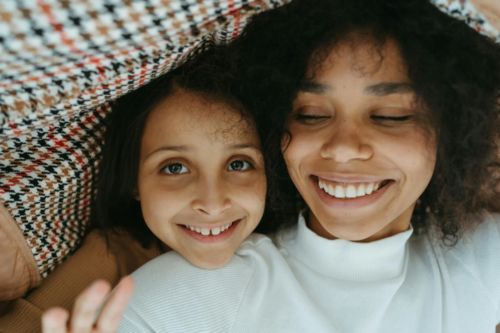 A mother and child laughing together under a checkered blanket.